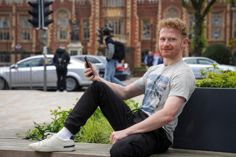 student sat outside one elmwood student centre looking at phone